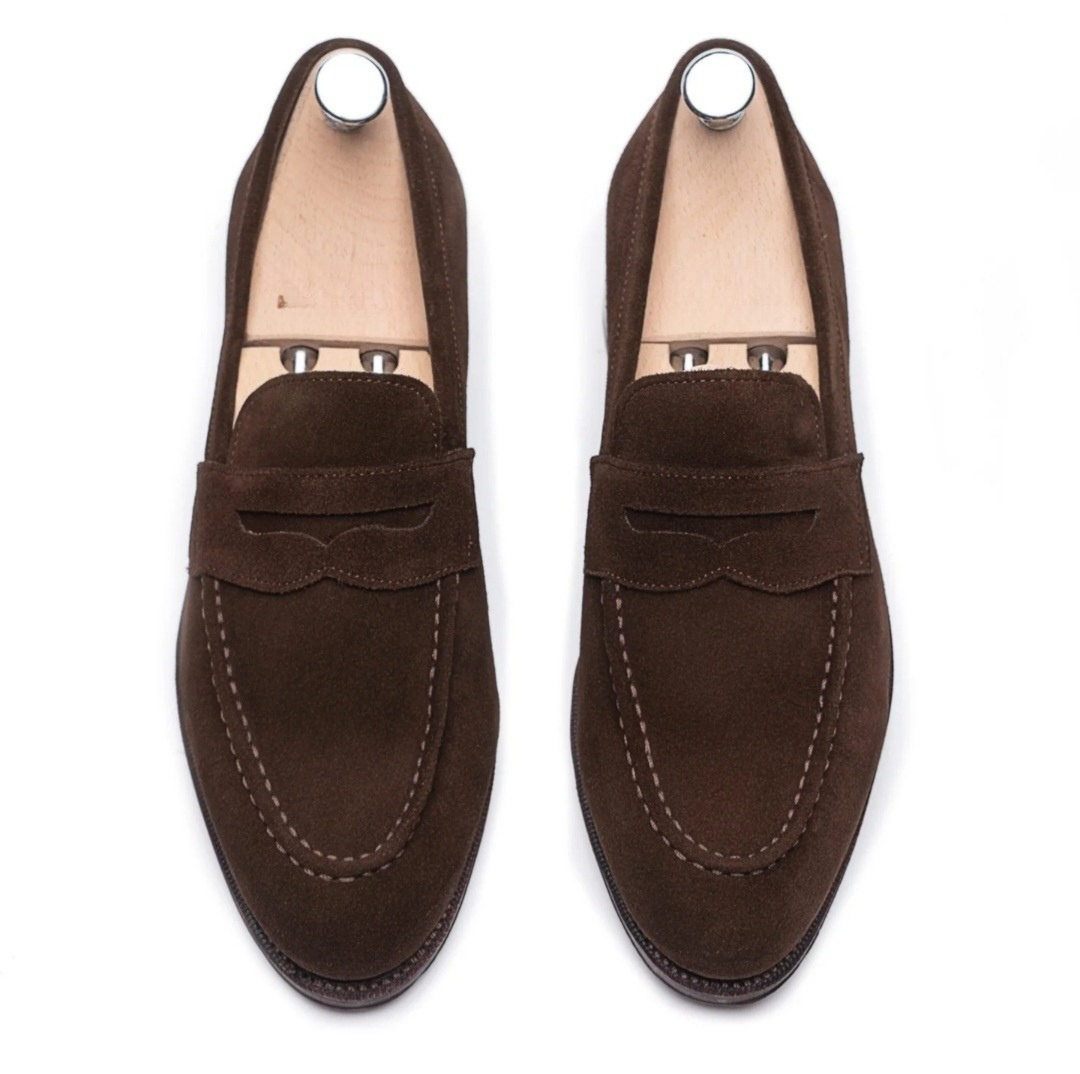 Pair of men's dark brown suede penny loafers with shoe trees, top-down view