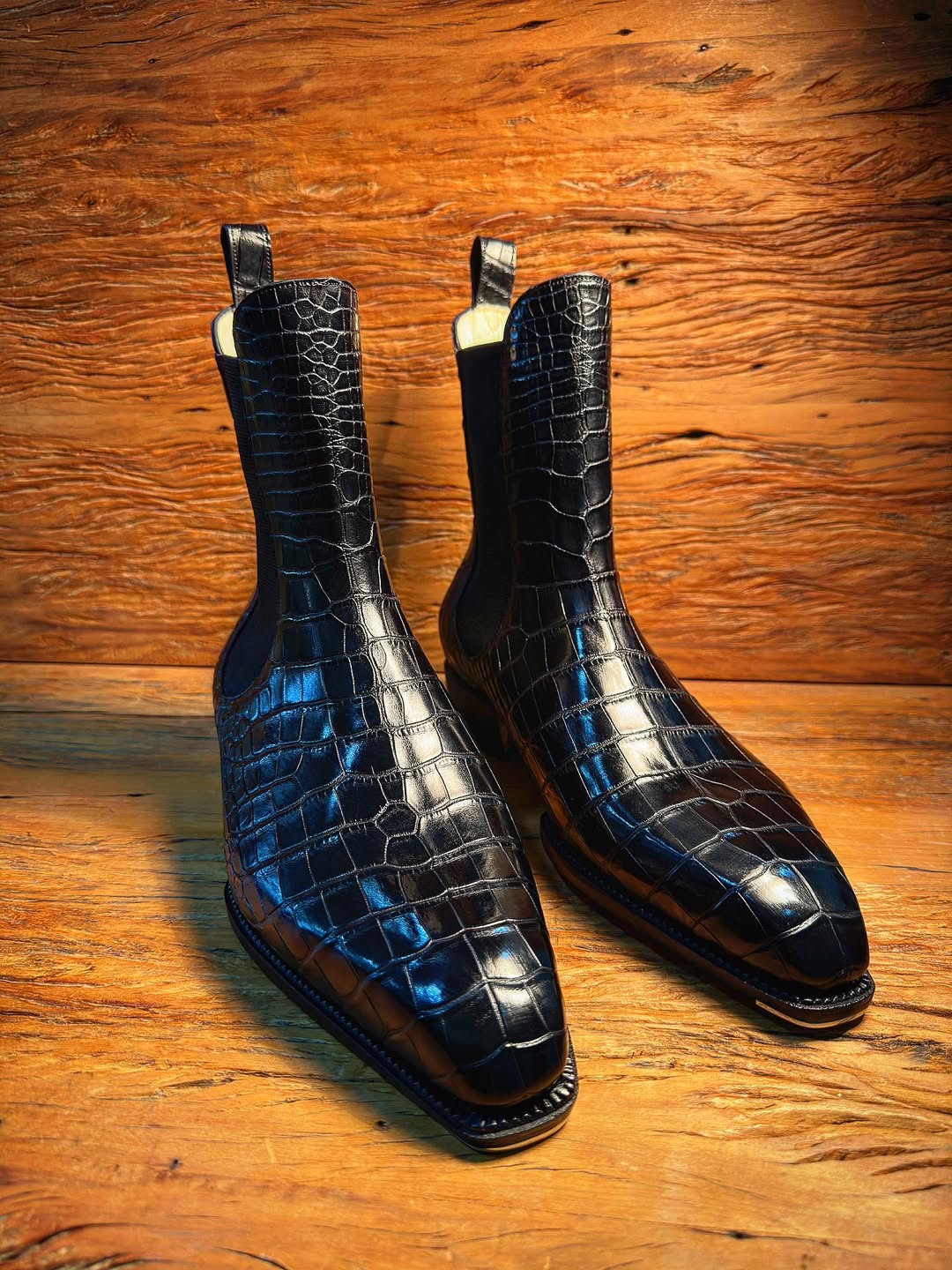 Pair of black crocodile skin boots on a wooden surface